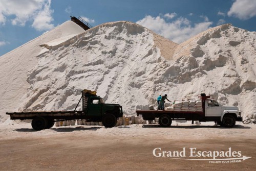 There, the salt is collected in artificially made pans. In the nearby plant it is cleaned from sand and then piled up in a huge pure white mountain, a majestic sight. It is finally scooped into bags of approx. 50 to 60 kilograms and then heaved onto trucks